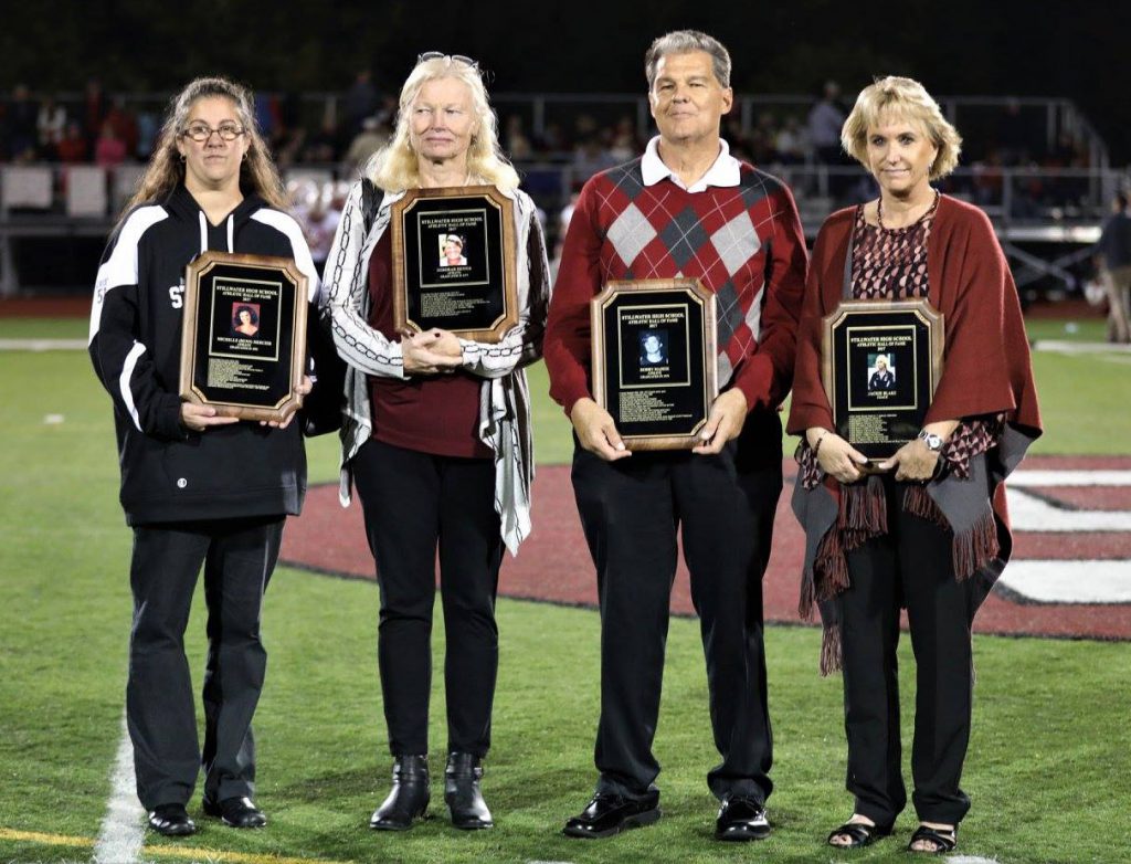 Four inductees standing together on the football field with plaques