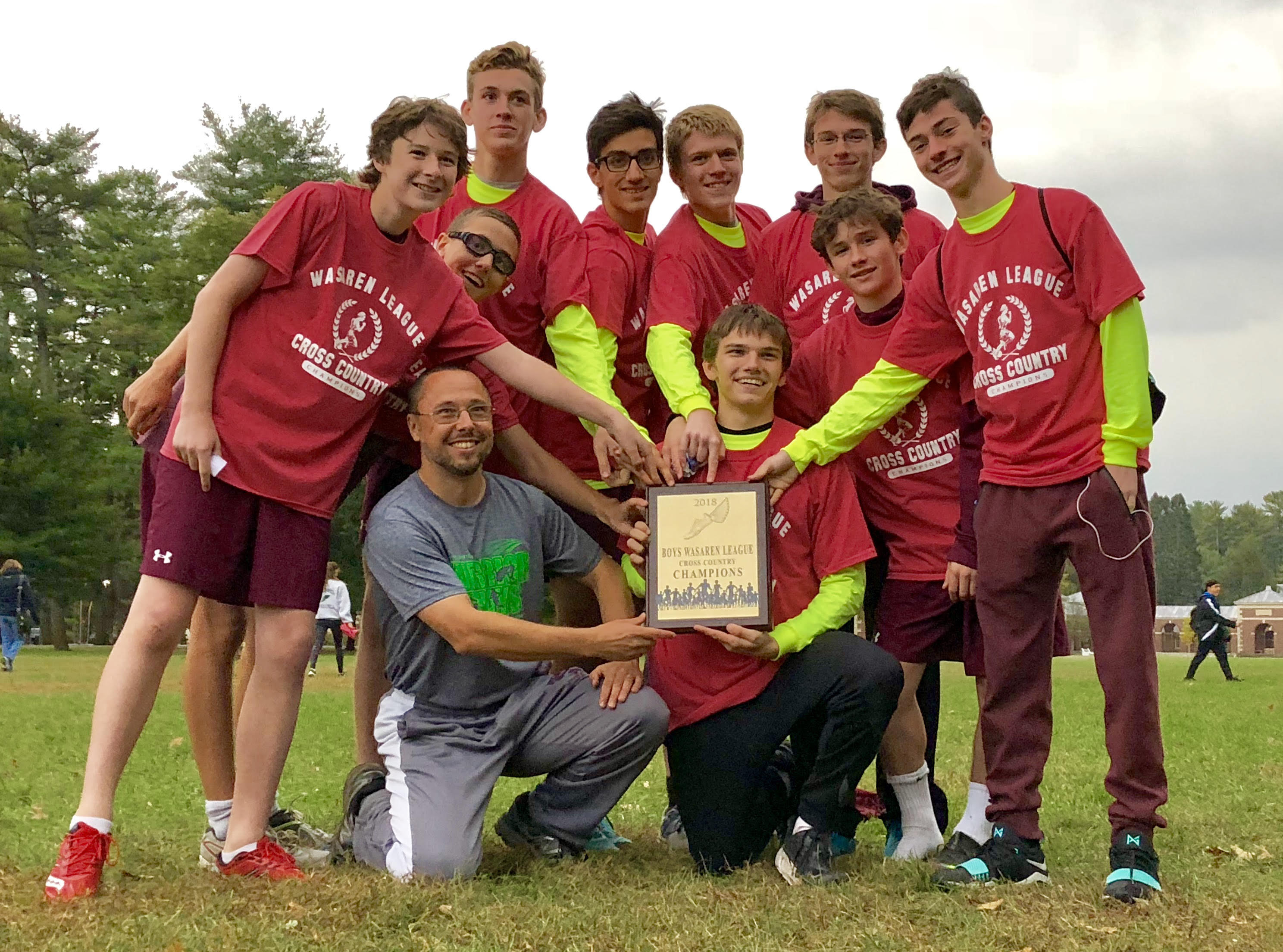 Cross country team huddled together with coach and trophy