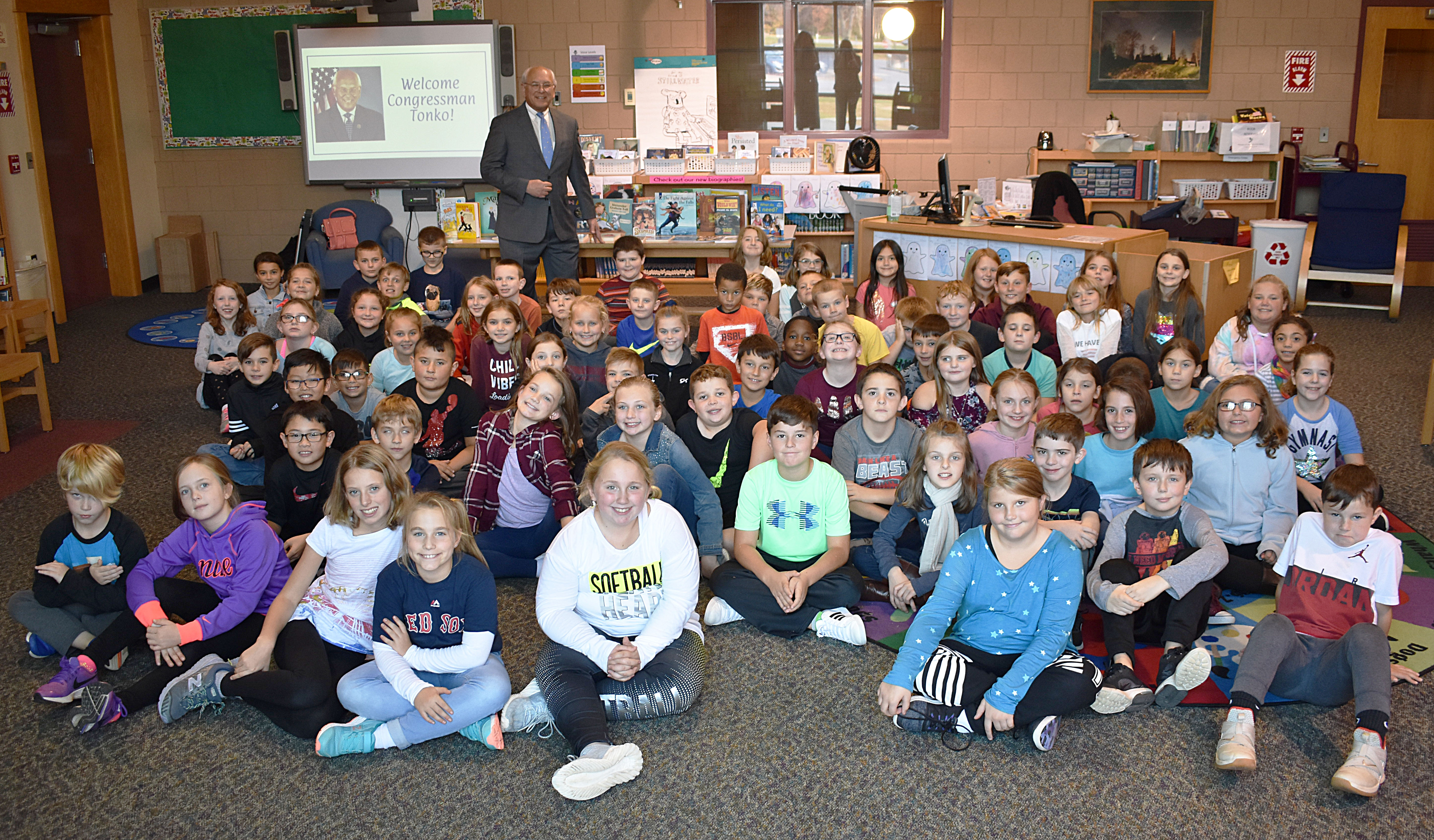 Congressman Paul Tonko stands behind fourth grade students sitting on the floor