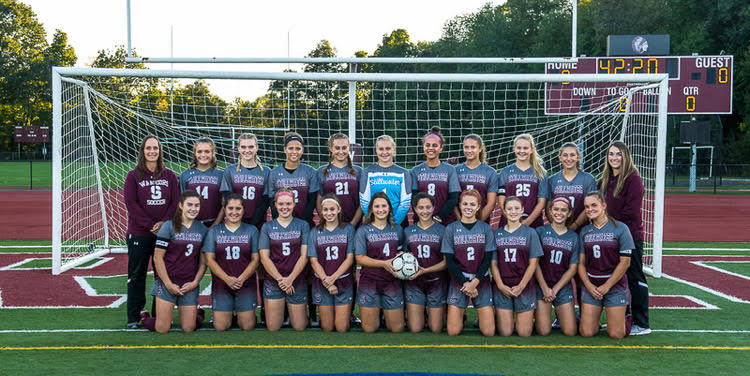 Girls varsity soccer team posing for a photo in front of a soccer goal