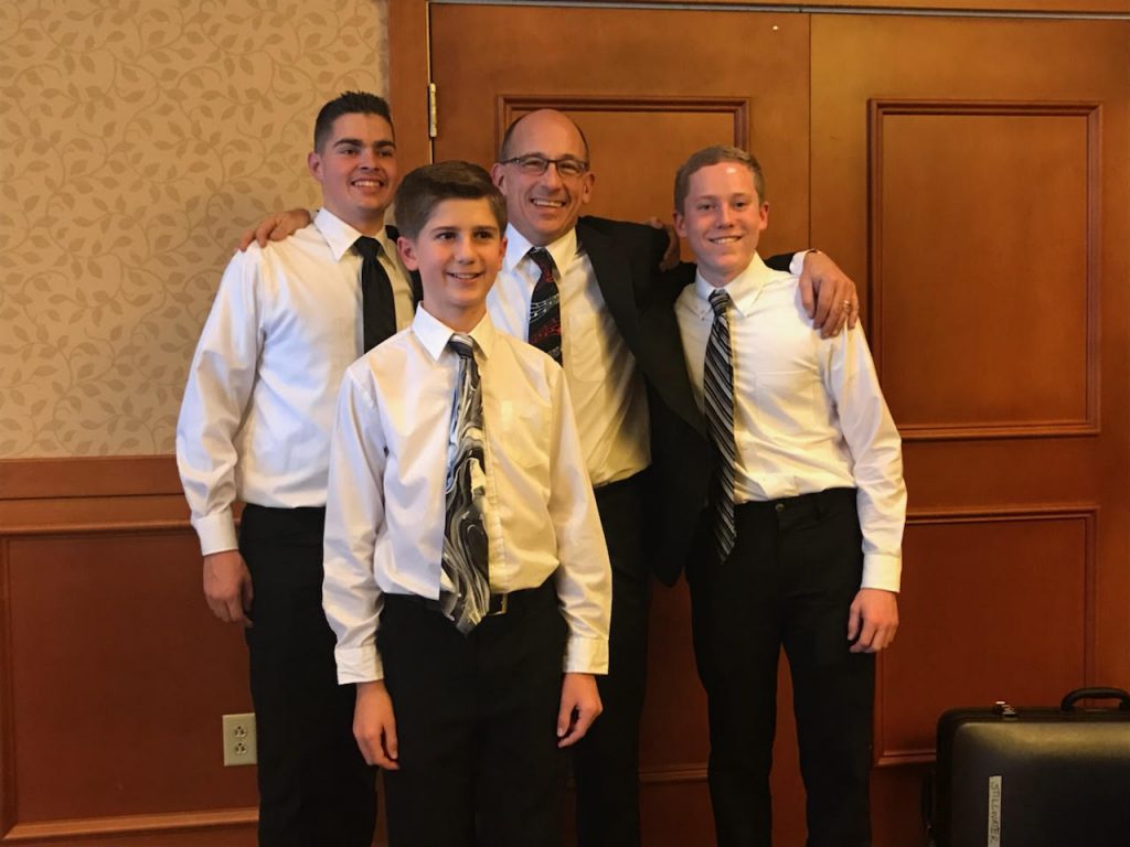 Three students stand and pose with teacher for a photo