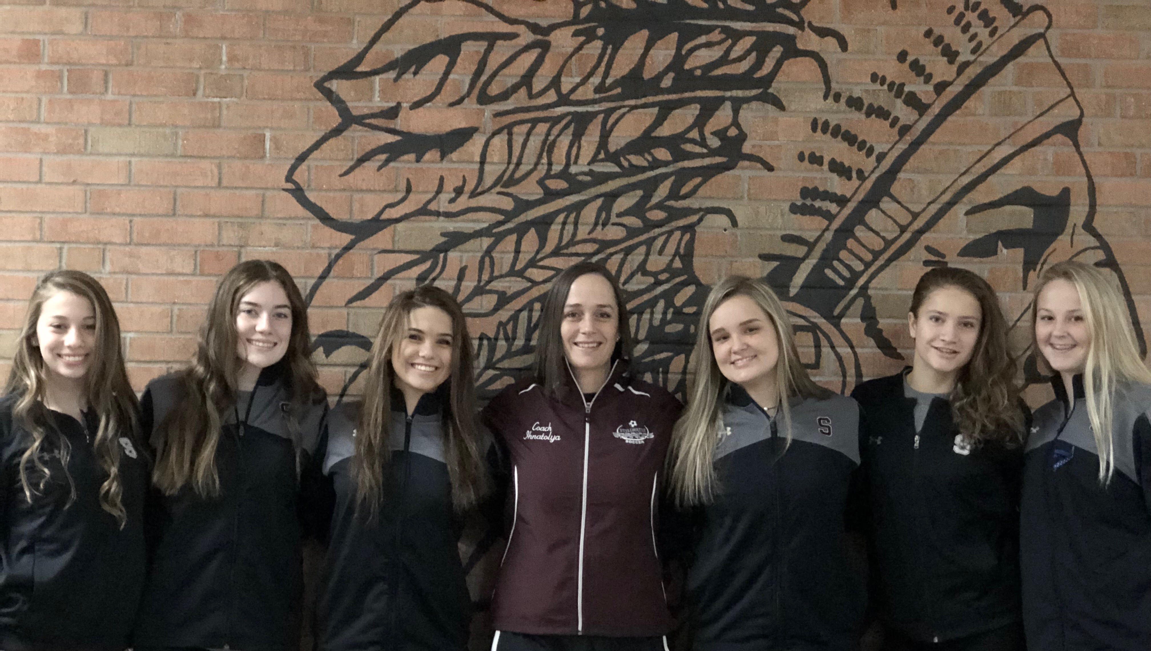 Members of the girls soccer team lined up in a row with their coach smiling 