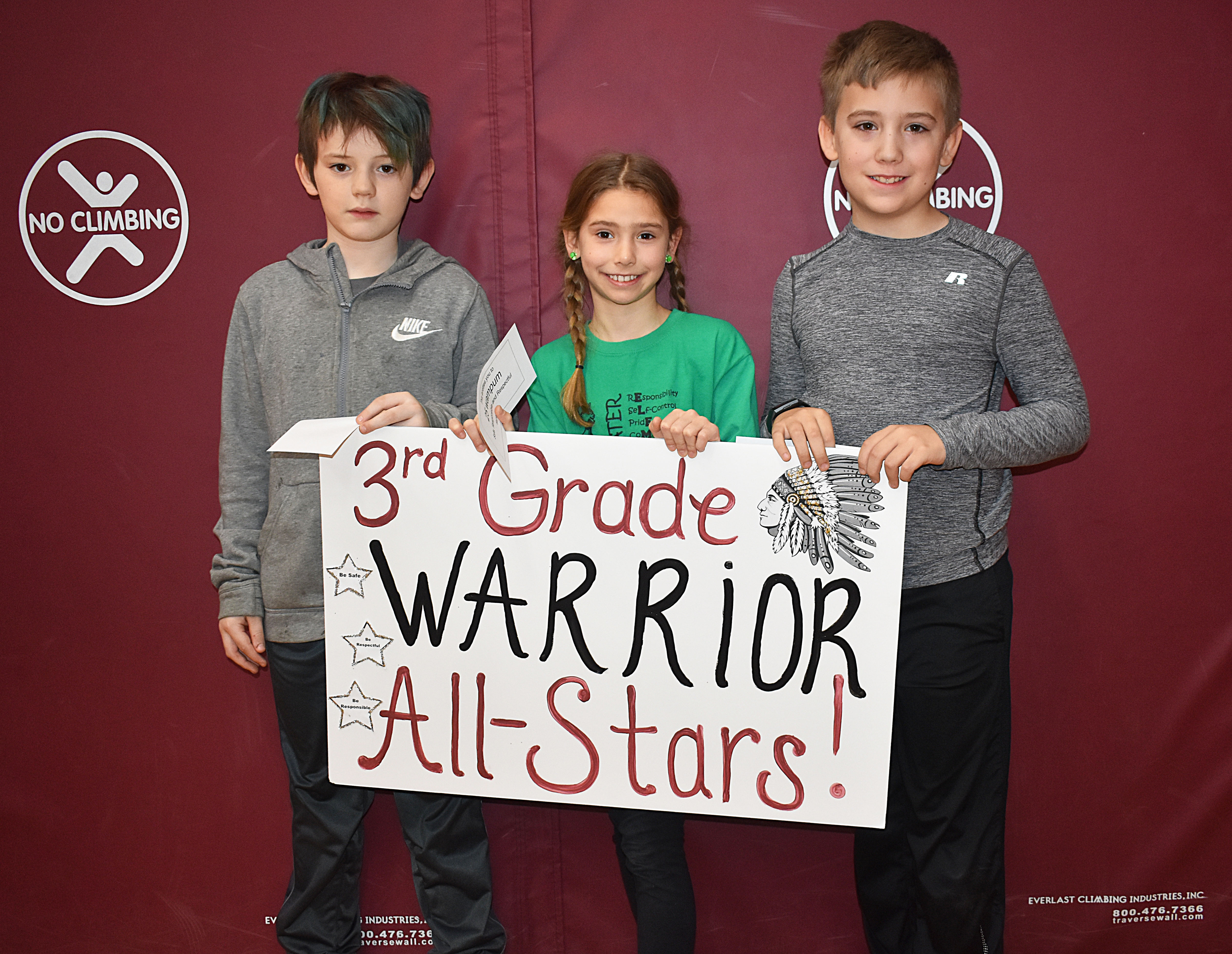 Three third graders gathered together with the third grade sign