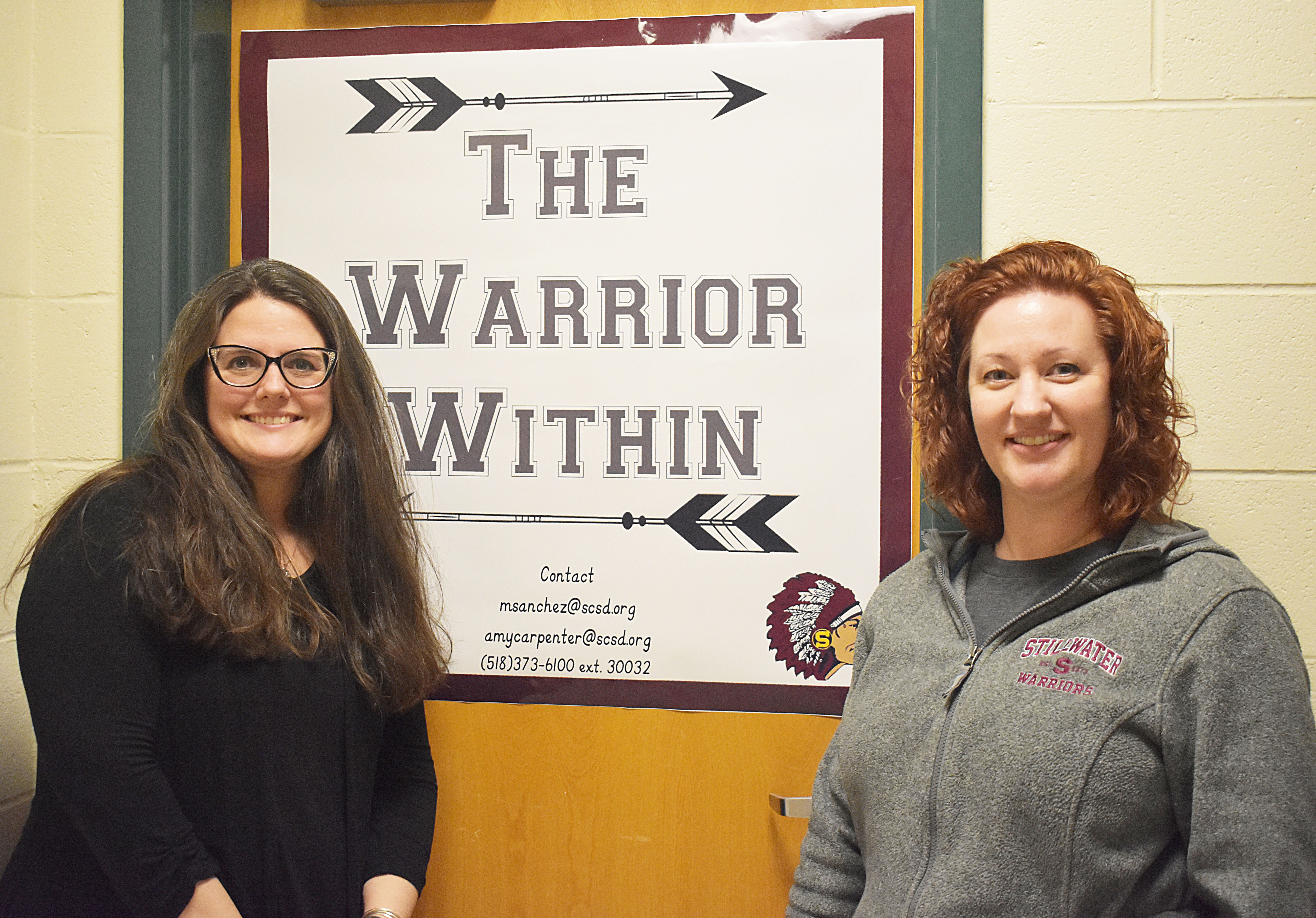 Librarian Amy Carpenter and Library Aide Megan Sanchez stand in front of Warrior Within sign 