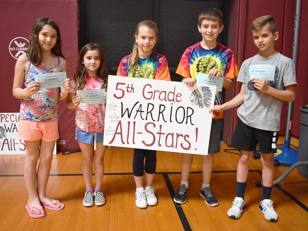 A group of students standing behind fifth grade sign