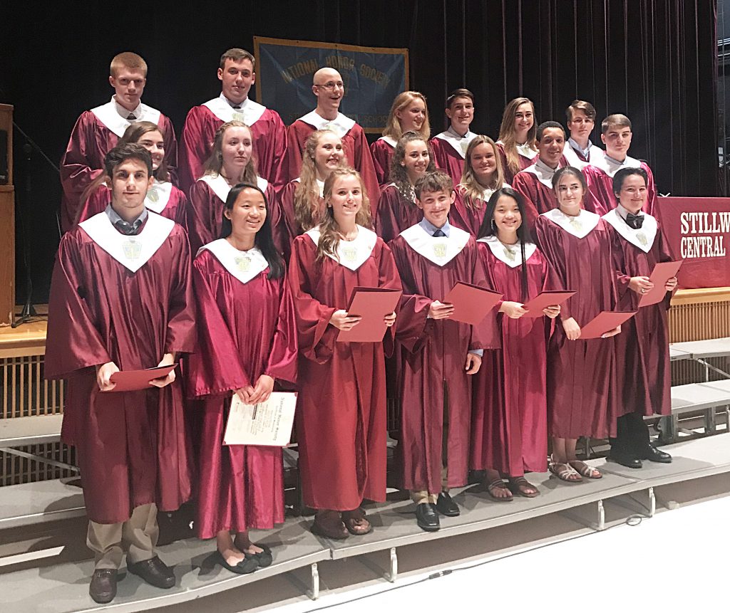Students lined up on risers in a group with maroon gowns on