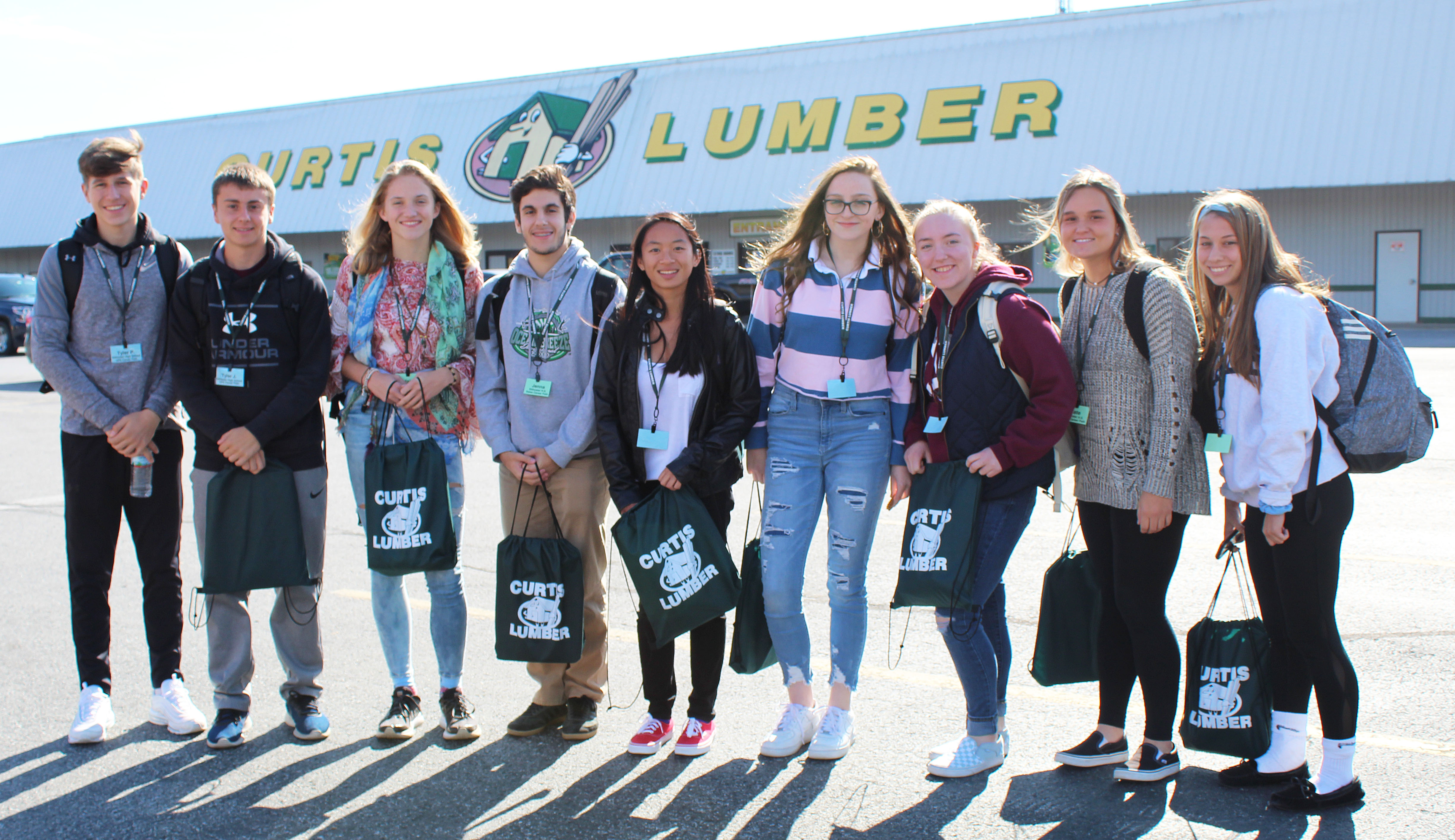 9 students lined up in front of Curtis Lumber store