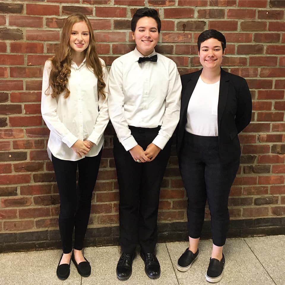 Three students standing together in front of a brick wall