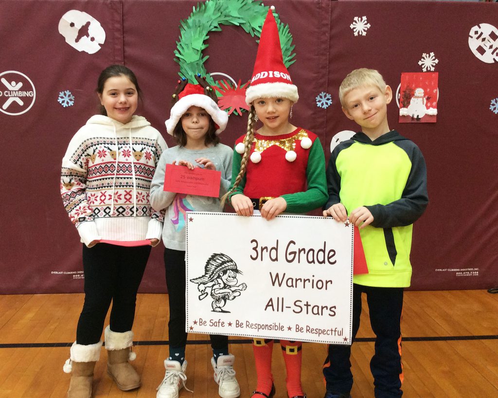 Four students standing with third grade warrior sign