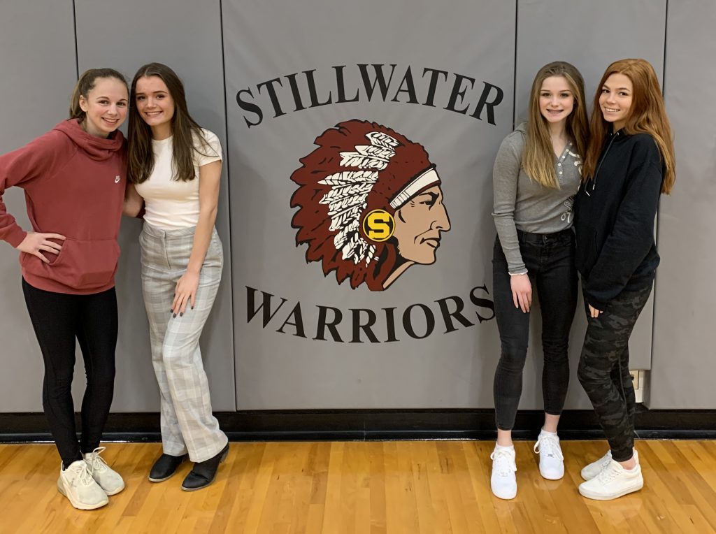 Four athletes standing in front of the Stillwater Warriors sign