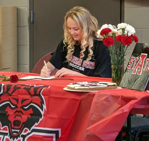 Student sitting at a table with a red table cloth signing a piece of paper