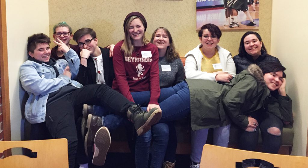 Group of 8 students gathered together on a bench smiling