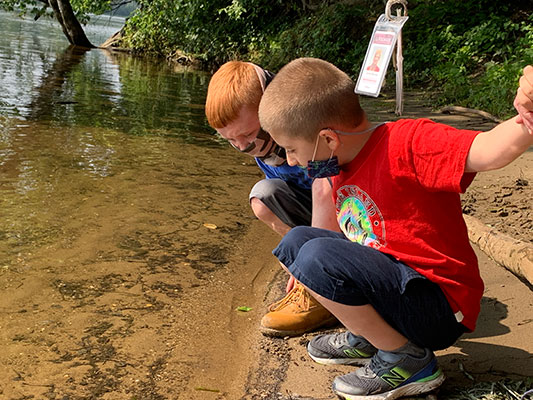 two students looking into the shoreline water of the Hudson River