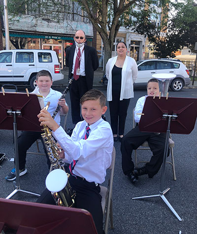 students seated holding instruments, teachers standing, outside