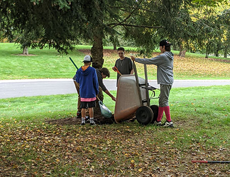 students with wheelbarrow and rakes under a tree