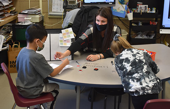 Madison Ramnes working with two students at a table