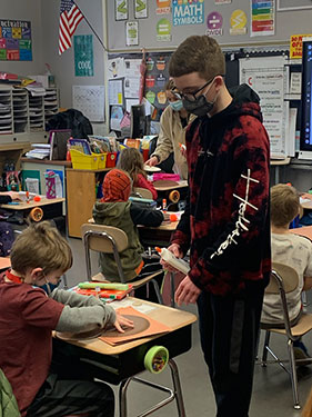 HS student working with 2nd grade student at their desk