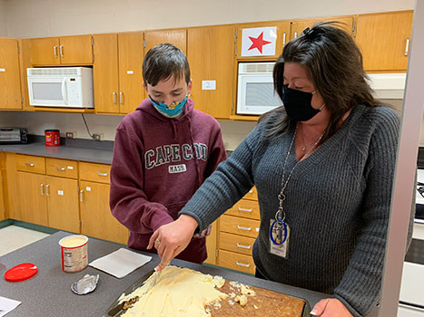 Angela cuts cake as student looks on