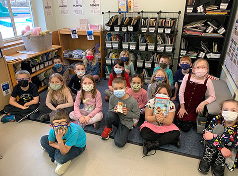 students in a group in classroom, one is holding a book