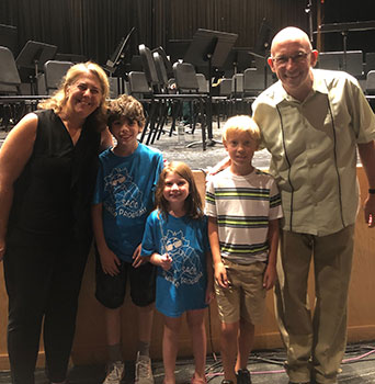 2 adults standing with 3 students with stage behind them