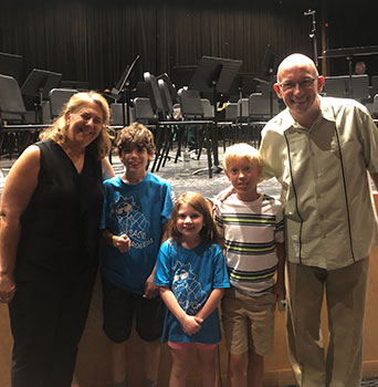 2 adults standing with 3 students with stage behind them