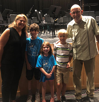 2 adults standing with 3 students with stage behind them