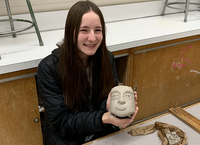 student holding clay pottery face