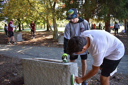 students scrubbing cemetery marker and raking