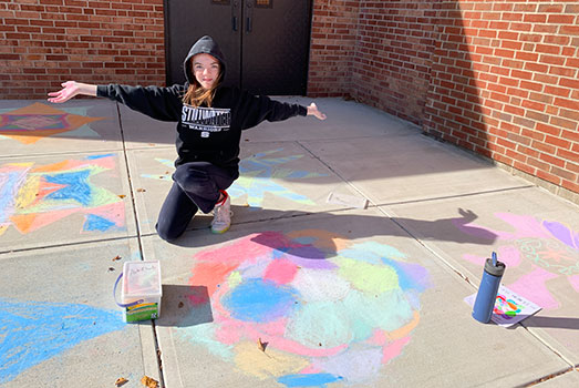 student kneeling near their rangoli design