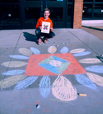 student sitting by their rangoli holding a diagram of it