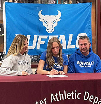 Kara signing letter at table as parents look on