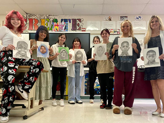 group of students and teacher holding portraits they created