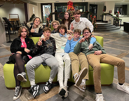 group of students seated and standing in hotel lobby, giving the peace sign