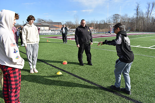 student wearing goggles walking a line while Officer Lyons and other students look on