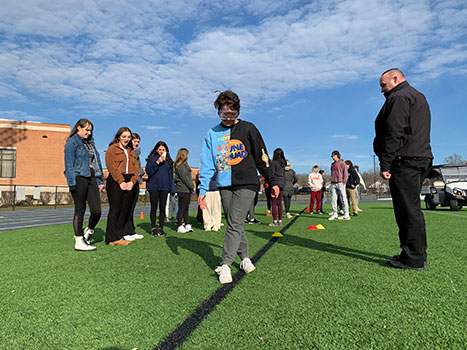 student wearing goggles walks a line while Officer Lyons and students look on