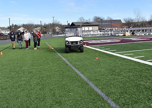 student driving golf cart while other students look on