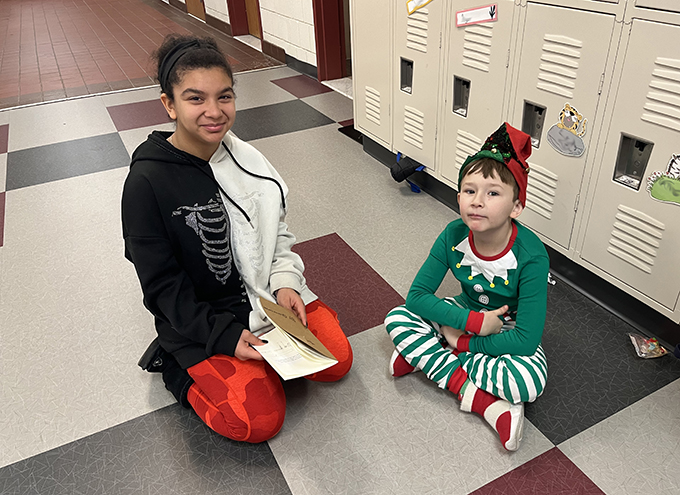 6th grade student sitting on floor with 3rd grade student