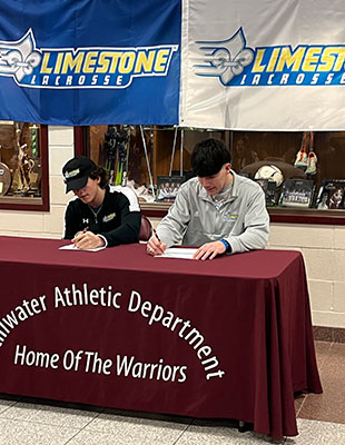 2 students signing letters at a table