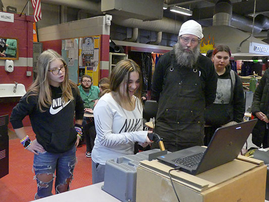 student works with virtual welder while teacher and other students look on