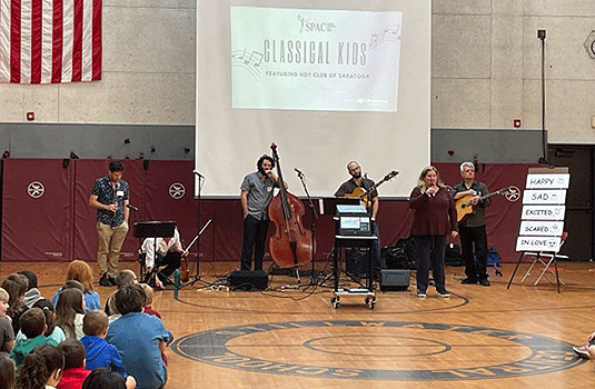 6 orchestra members speaking to students in the gym