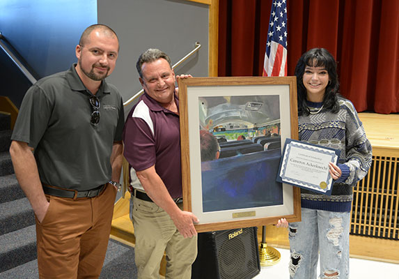 Roman Garasymchuk, Transportation Advisor, Leonard Bus Sales, Inc. standing with Tom Murphy, Director of Transportation and Cameron holding the painting and award certificate.