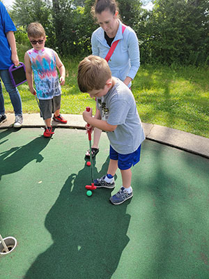 student hitting a mini golf ball on the green