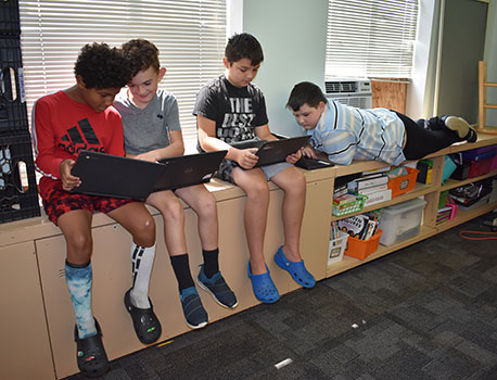 4 students sitting in front of a window looking at laptops