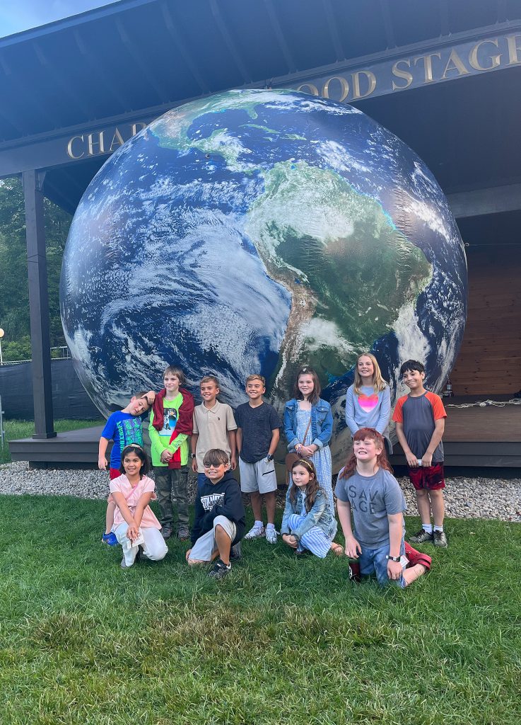 A group of students smiling for a photo by a giant globe.
