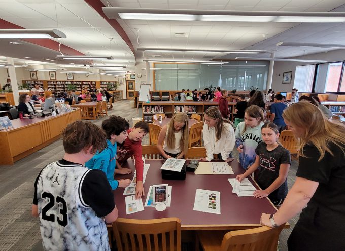 Students and a teacher review materials at a table.