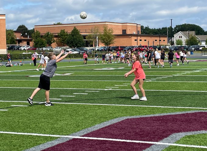 Two students playing volleyball on the turf field.