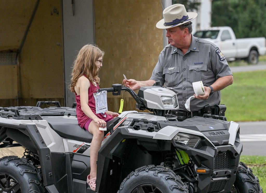 NYS Trooper handing a sticker to a little girl sitting on an ATV.