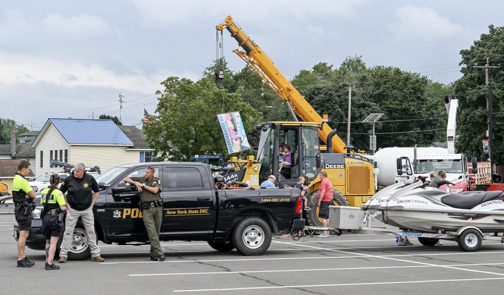 Various trucks and trailers are parked in the school parking lot as people walk around to view them.