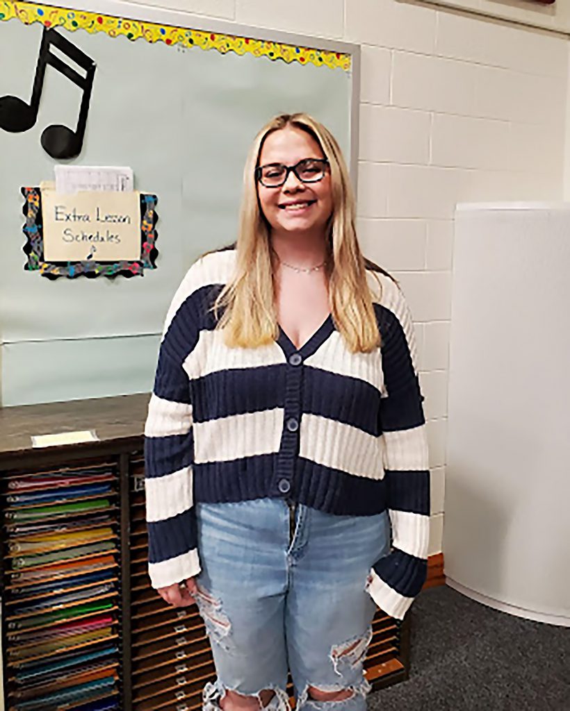 Student smiling for a photo in front of a music bulletin board.