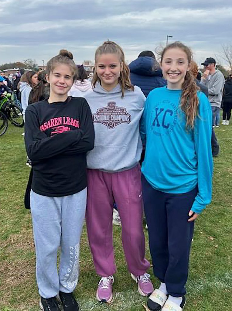 Three members of the girls cross country team smiling for a group photo.